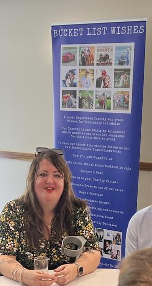 A member seated beside the Bucket List Wishes display board