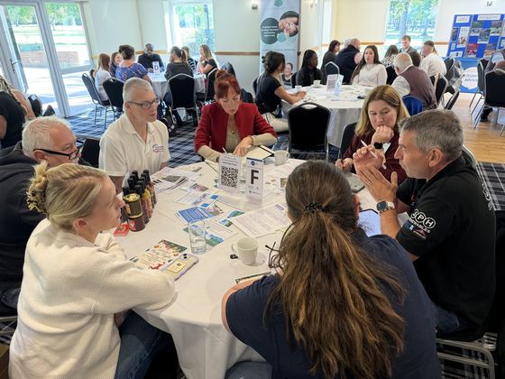 A busy table of members swapping ideas over leaflets and hot sauce