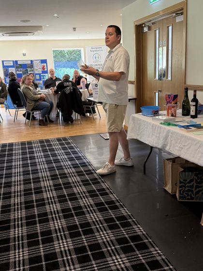 An organiser speaking to the room beside the raffle prizes